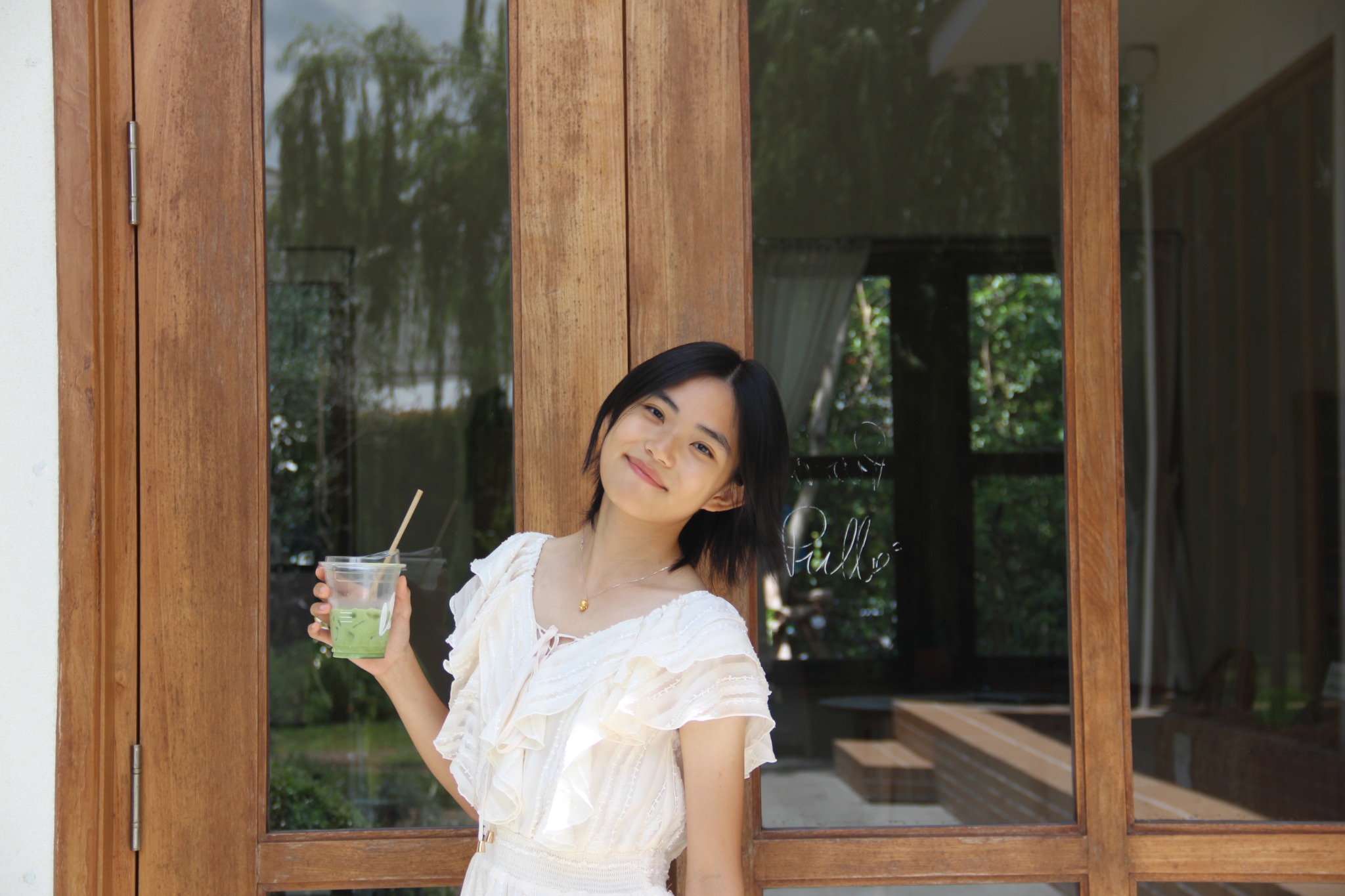 Sisley smiling and holding an iced matcha by wooden doors